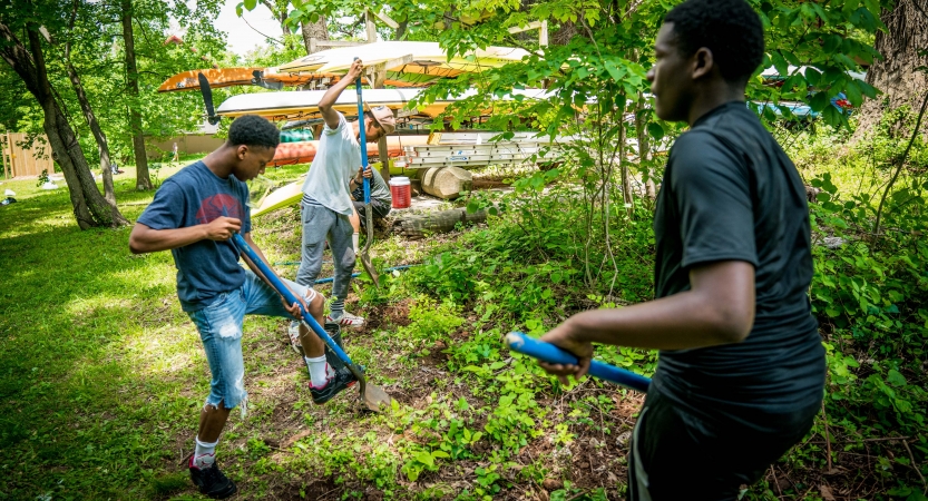 Three people use tools in a wooded area during a service project. 